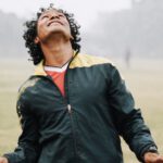 Soccer Shot - Smiling football male player with curly hair wearing sportswear hitting soccer ball with head while playing on field